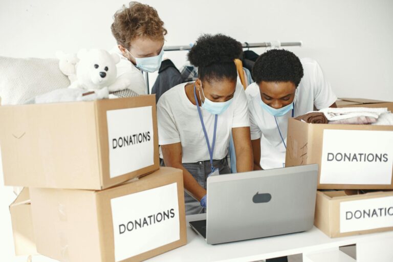 Group of volunteers wearing masks sorting donations with a laptop, promoting diversity and teamwork.