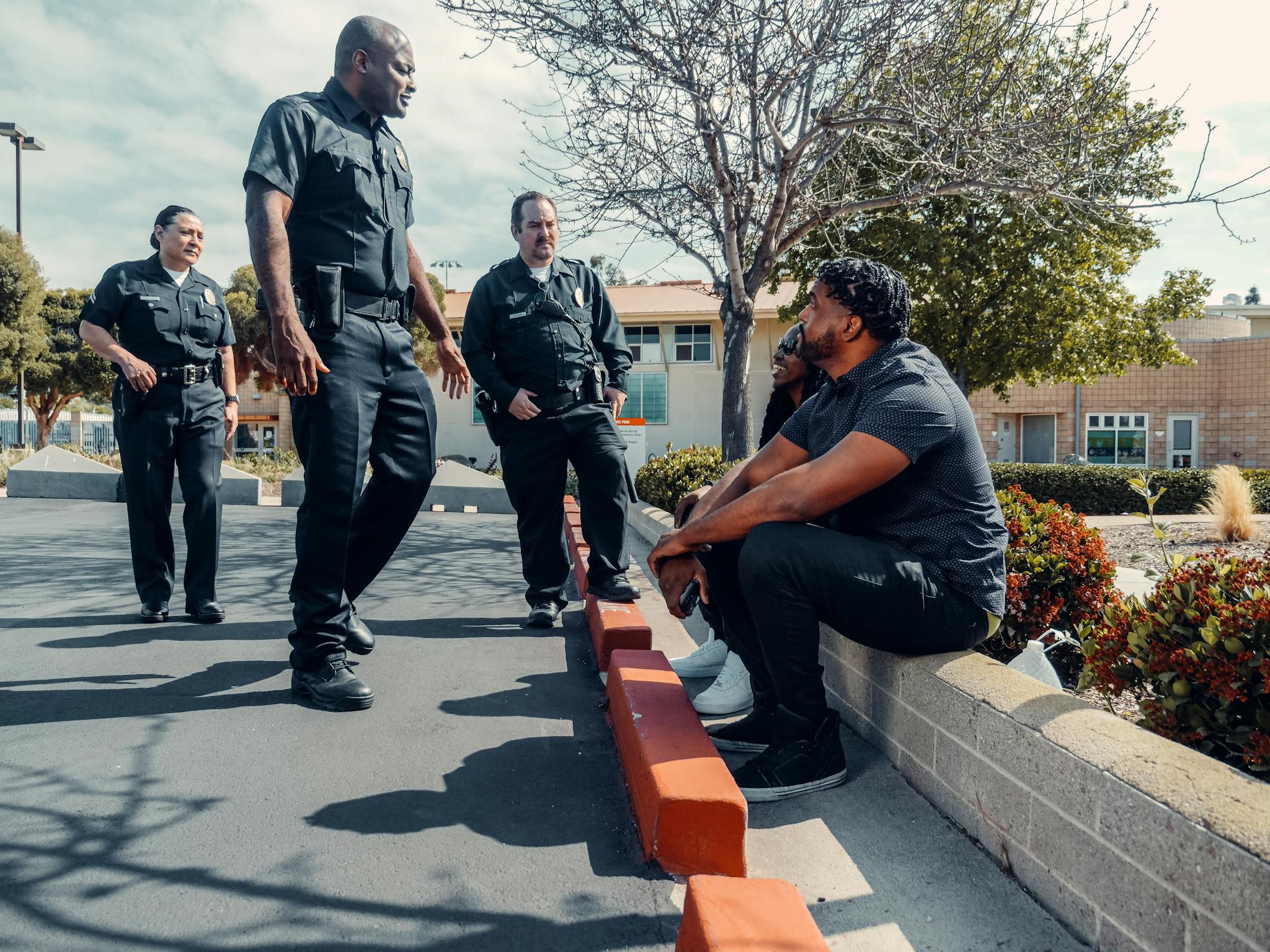 Police officers interacting with individuals seated outdoors in a parking area.